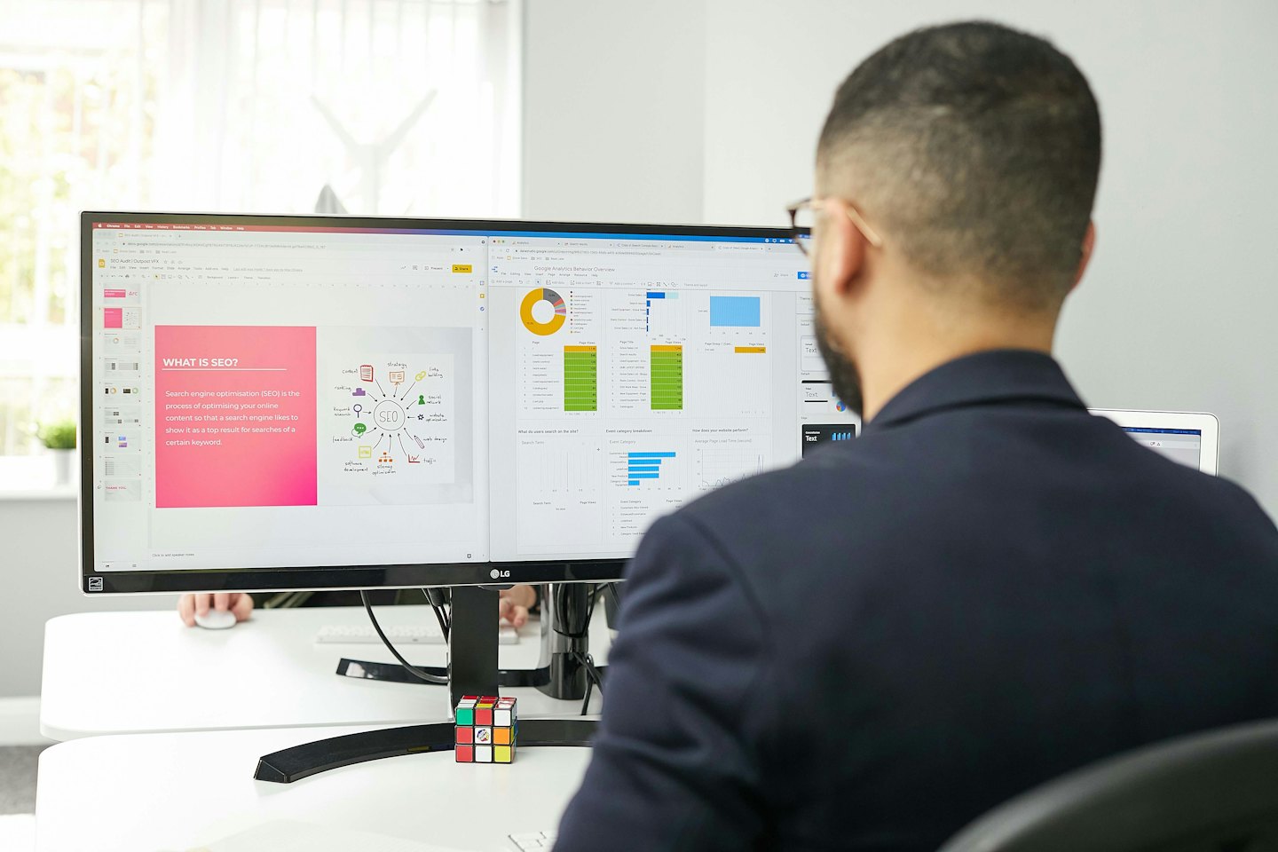 Muž pracuje na dvou monitorech počítače zobrazujících SEO a analytiku.